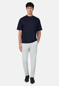 Marineblaues T-Shirt mit kurzen Ärmeln, kombiniert mit hellgrauen Hosen und schwarzen Turnschuhen, mit lockerem Schnitt und glatter Stoffstruktur.