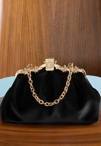 Geantă de mână din catifea neagră cu mânere din lanț aurit. Prezintă accesorii aurii ornate cu accente florale și închidere cu știft. Textură netedă.