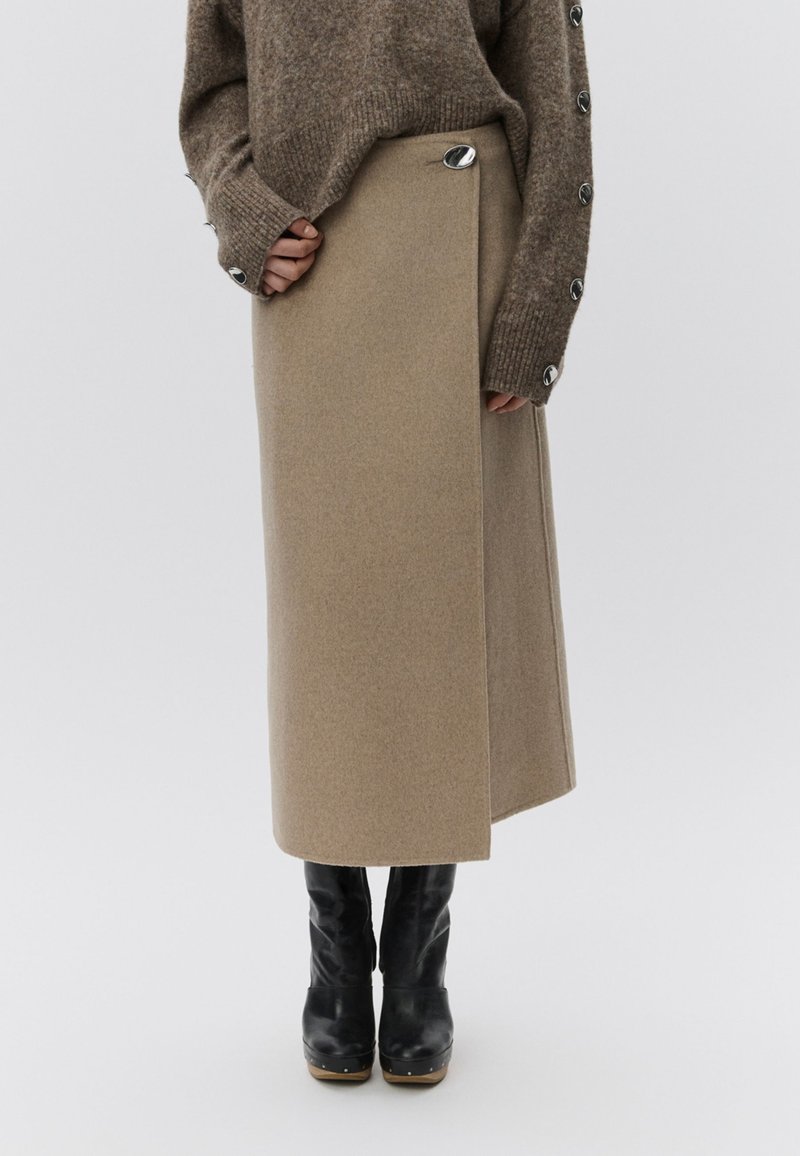 Ζακάρ φούστα σε ανοιχτό μπεζ χρώμα με μεταλλικό ασημί κουμπί. Συνδυασμένη με μαύρες δερμάτινες μπότες μέχρι το γόνατο. Απαλή υφή, μήκους μέχρι το γόνατο.