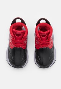 Czerwone i czarne sportowe trampki o błyszczącym wykończeniu, z wyściełanym kołnierzem, zaokrąglonym kształtem i teksturowaną gumową podeszwą. Wyposażone w pętelki ułatwiające zakładanie.