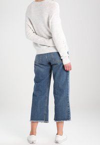 Maglione grigio chiaro con orlo e polsini a coste, abbinato a jeans azzurri a gamba larga con orli sfrangiati e tasche posteriori. Indossato con sneakers bianche.