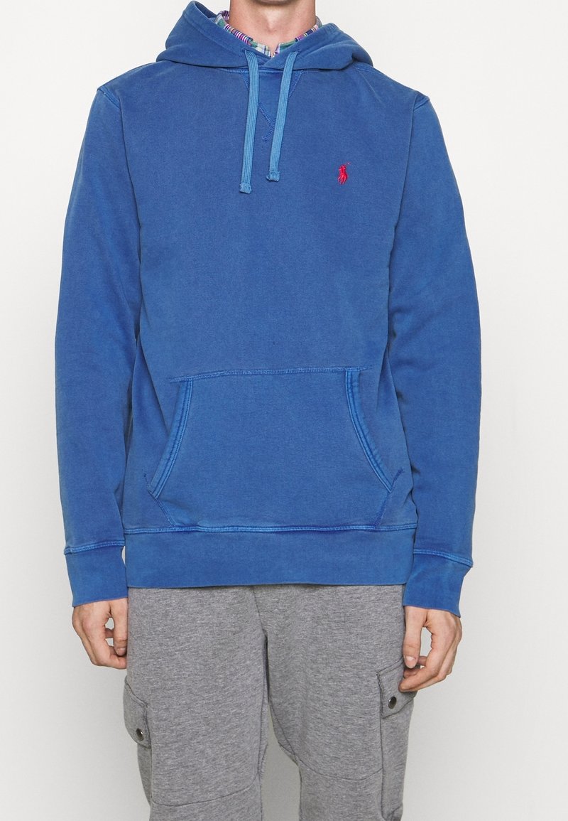 Sudadera de algodón azul con bolsillo canguro frontal, capucha con cordón y logo rojo en el pecho. Presenta puños y dobladillo acanalados.