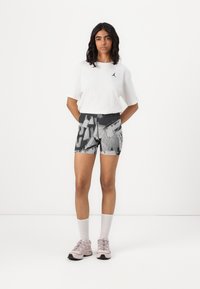 Shorts med ett svartvitt geometriskt mönster; kombinerat med en vit T-shirt som har en liten logotyp. Bärs med rosa sneakers och grå strumpor.