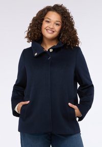 Cappotto in lana blu navy con colletto alto, dotato di chiusura a bottoni color oro, due tasche laterali e una finitura liscia e strutturata.