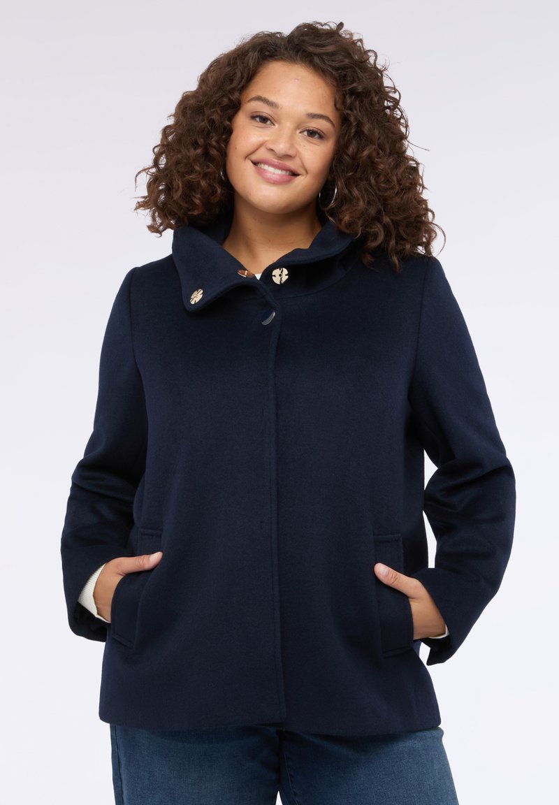 Cappotto in lana blu navy con colletto alto, dotato di chiusura a bottoni color oro, due tasche laterali e una finitura liscia e strutturata.
