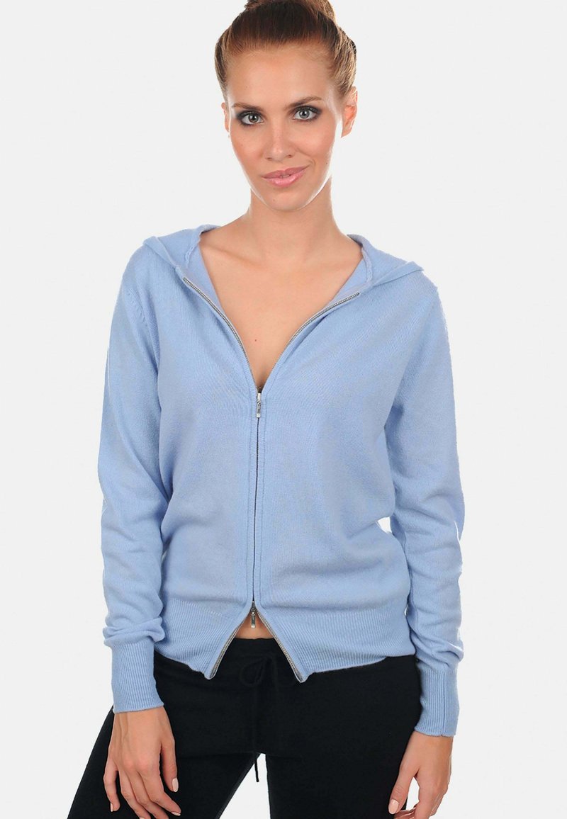 Haut à fermeture éclair bleu fabriqué en tissu doux, doté d'une capuche, de poignets côtelés et d'un design à ourlet fendu. Texture lisse sans motifs visibles.