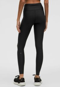 Leggings negros de cintura alta con una textura suave y elegante y un sutil detalle de logo cerca del tobillo. Presentan un diseño ajustado adecuado para ropa activa.