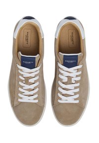 Beiga mockasinsneakers med vita snören, rund tå och en kontrasterande marinblå etikett på tungan. Slät inredning och gummisula.