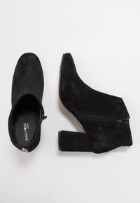 Sorte suede ankelstøvler med spids tå, kraftig hæl og lynlåsdetalje i siden. Glat tekstur og minimalistisk design.