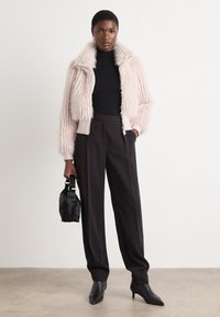 Faux fur jas in zacht roze, met een ritssluiting en geribbelde manchetten. Zwarte coltrui, hoge zwarte broek en een kleine tas maken de look compleet.