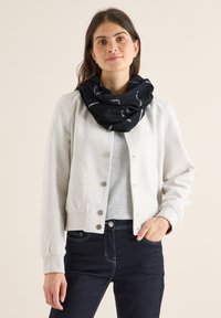 Veste bomber zippée gris clair avec une texture douce, dotée de boutons-pression et de poignets côtelés. Une écharpe infinity à motifs noirs apporte du contraste.