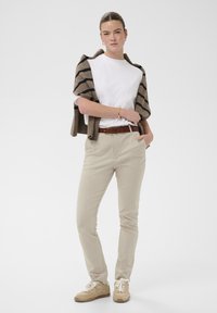 Pantalons kaki avec une coupe ajustée, associés à un t-shirt blanc et un cardigan rayé brun. Portés avec des baskets beiges et une ceinture marron.