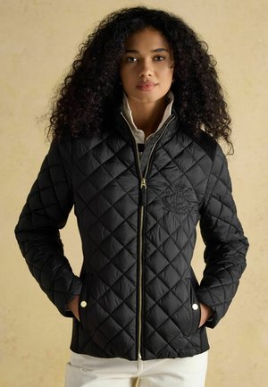Black quilted jacket with a zip closure, featuring a logo on the chest, side pockets, and a soft texture. Accented with gold hardware.