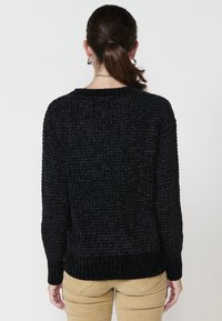 Črni pleteni pulover z teksturiranim vzorcem, rebrastimi manšetami in robom ter okroglo izrezano ovratnikom. Zadnji pogled prikazuje sproščen kroj.