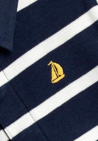 Sötétkék póló fehér vízszintes csíkokkal és egy kis hímzett sárga vitorlás logo-val a bal oldalon. Pamut szövet textúra.