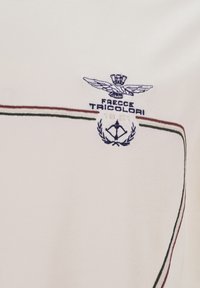 Camicia di cotone bianca con logo ricamato raffigurante un'aquila, "Frecce Tricolori", e un emblema datato, accentuata da linee verdi, bianche e rosse.
