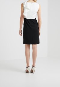 Robe noir et blanc avec une forme structurée ; le haut blanc présente un accent froncé ; tissu lisse ; longueur au genou, fermeture éclair au dos.
