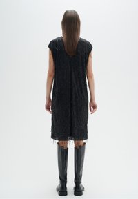 Černé bezrukávové šaty s vertikálními flitry, surovým lemem a jemnými třásněmi. V kombinaci s černými koženými vysokými botami až ke kolenům.