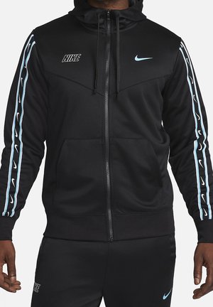 Sort Nike lynlås-hættetrøje og matchende bukser med lyseblå swoosh-logoer på bryst, ærmer og ben, båret af en person.