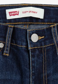 Levi's 510 skinny jeans i mörkblå denim, med en vit etikett med röd text, gula sömmar och en metallknappsstängning.