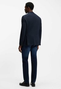 Granatowa teksturowana marynarka na jedno zapięcie, zestawiona z ciemnymi dżinsami i czarnymi skórzanymi butami, widziana od tyłu.