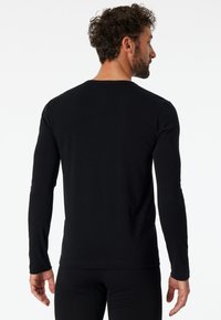 Zwarte langwerpige T-shirt met lange mouwen, gemaakt van katoen, met een ronde hals en een getailleerde pasvorm, met een gladde textuur en geen zichtbare patronen of accenten.