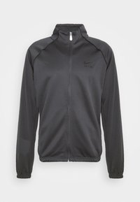 Giacca nera con zip realizzata in tessuto liscio. Presenta un colletto alto, maniche lunghe, polsini a coste e un piccolo logo Nike sul petto.