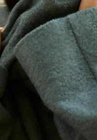 Zelená, texturovaná látka s měkkým, chlupatým povrchem. Materiál vypadá silně a je uspořádán v záhybech, čímž zdůrazňuje své splývavé vlastnosti.