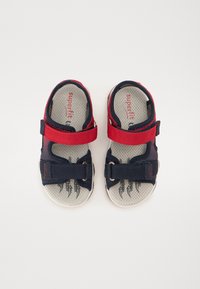 Kinder-Sandalen mit navyblauem Stoff, roten Klettverschlüssen, offenem Zehendesign und gepolsterten Innensohlen mit rutschfestem Griff.