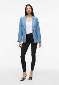 Svetlomodrý blazer so štruktúrovaným dizajnom, jednostranným zapínaním na gombík a dlhými rukávmi, kombinovaný s čiernymi slim-fit džínami a čiernymi lodičkami.