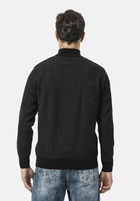 Zwarte geribde trui met een hoge kraag en lange mouwen, met een gemêleerd breipatroon. Gecombineerd met vervaagde blauwe jeans.