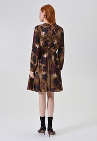 Langemouwen jurk met een getailleerde taille en een uitlopende rok, met een bruin en bordeauxfloraal patroon op een zijden stof.