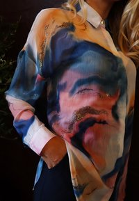 Többszínű selyemblúz kék, rózsaszín és arany mintákkal, gallérral, hosszú ujjal és zsebbel. Puha tapintású és könnyű kialakítású.