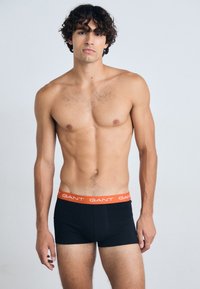 Zwarte boxershorts met een oranje tailleband met het "GANT" logo. Het model heeft een atletisch figuur en is shirtloos. Eenvoudig, minimalistisch ontwerp.