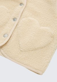 Crème-kleurige fleece stof met hartvormige zak en drukknoopjes langs de afgewerkte naad.