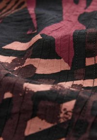 Textil med abstrakta mönster i djup röd, svart och persika. Materialet är troligtvis lätt och har en subtil textur.