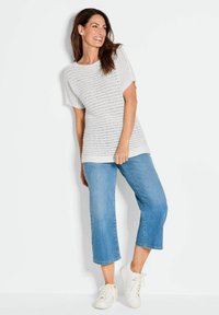 Lichtgrijze gebreide top met gestructureerde strepen, gecombineerd met verkorte blauwe denim broeken en witte sneakers. Losse fit en korte mouwen.