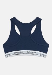 Sutiã desportivo com alças nadador em azul marinho da Calvin Klein, com uma faixa elástica branca com a marca na parte inferior, exibido de forma plana sobre um fundo claro.