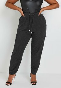 Svarta sweatpants med en texturerad, prickig mönster, elastiska muddar, dragsko i midjan och sidofickor, tillsammans med svarta högklackade skor.