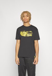 Sort bomuld t-shirt med et gult grafisk print med "Puma" logo. Rund hals og korte ærmer, parret med mørke bukser.