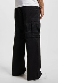 Pantalons cargo noirs avec une coupe décontractée, dotés de poches latérales et d'un tissu doux et texturé. Le design comprend des détails plissés et des jambes larges.