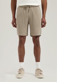 Beige bomullsshortser med elastisk snor i midjen, kne-lange, teksturert stoff, kombinert med kremfargede sneakers og hvite sokker.
