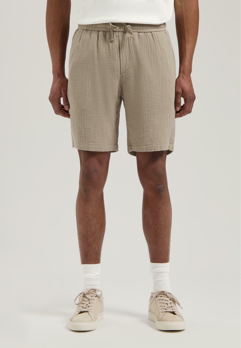 Beige bomullsshortser med elastisk snor i midjen, kne-lange, teksturert stoff, kombinert med kremfargede sneakers og hvite sokker.