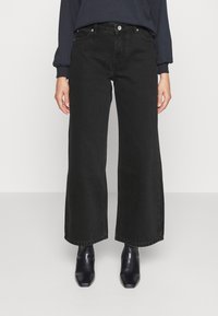 Musta leveälahkeinen farkut, joissa on korkea vyötärö, yksinkertaiset etutaskut sekä hopeanväriset napit ja niitit. Yhdistetty mustiin saappaisiin.