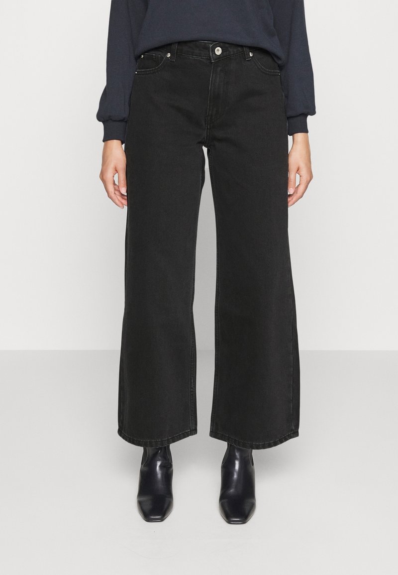 Musta leveälahkeinen farkut, joissa on korkea vyötärö, yksinkertaiset etutaskut sekä hopeanväriset napit ja niitit. Yhdistetty mustiin saappaisiin.