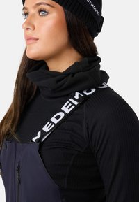 Sort ribbet turtleneck under navy bibshorts med en logo-strop. Turtleneck'en har en blød, tekstureret overflade, og bibshortsene har lynlåslommer.
