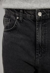Sorte denimjeans med en glatt tekstur, som har en metallknapplukking, sidelomme og klassisk fem-lomme design.