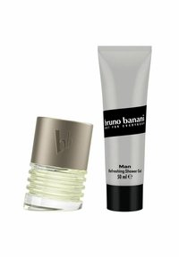 Tuoksupullo, jossa on teksturoidulla metallikorkilla varustettu kirkas pohja; sen vieressä hopeinen suihkugeelituubi mustilla yksityiskohdilla, jossa on "bruno banani" -merkintä.