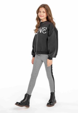 Schwarzer Pullover mit "LOVE" aus Pailletten, Puffärmeln, kombiniert mit karierter Leggings und schwarzen Schnürstiefeln. Die Outfits weisen kontrastierende Akzente auf.