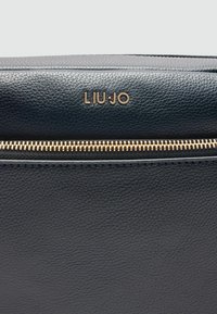 Schwarze strukturierte Lederhandtasche mit goldfarbener Reißverschluss und dem Logo "LIU:JO", das prominent oben angebracht ist. Sie verfügt über eine glatte Oberfläche.